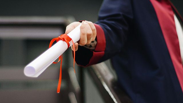 Person hält weiße Schriftrolle mit oranger Schleife in der Hand